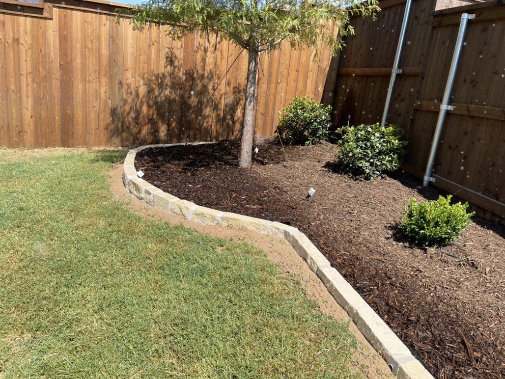 Stone-edged mulch bed with hollies and boxwood along a cedar fence