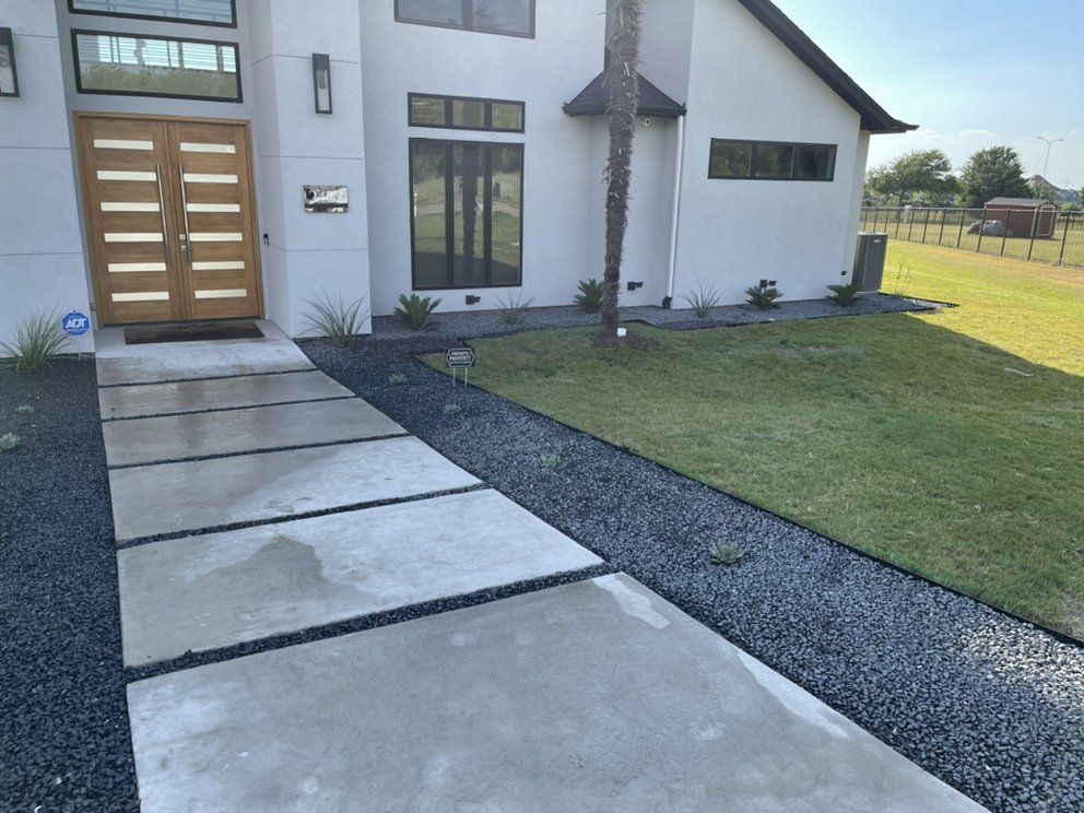 New front-yard landscape by JIT Landscape & Design in McKinney: floating concrete walkway, black Tejas gravel beds with steel edging and fresh sod